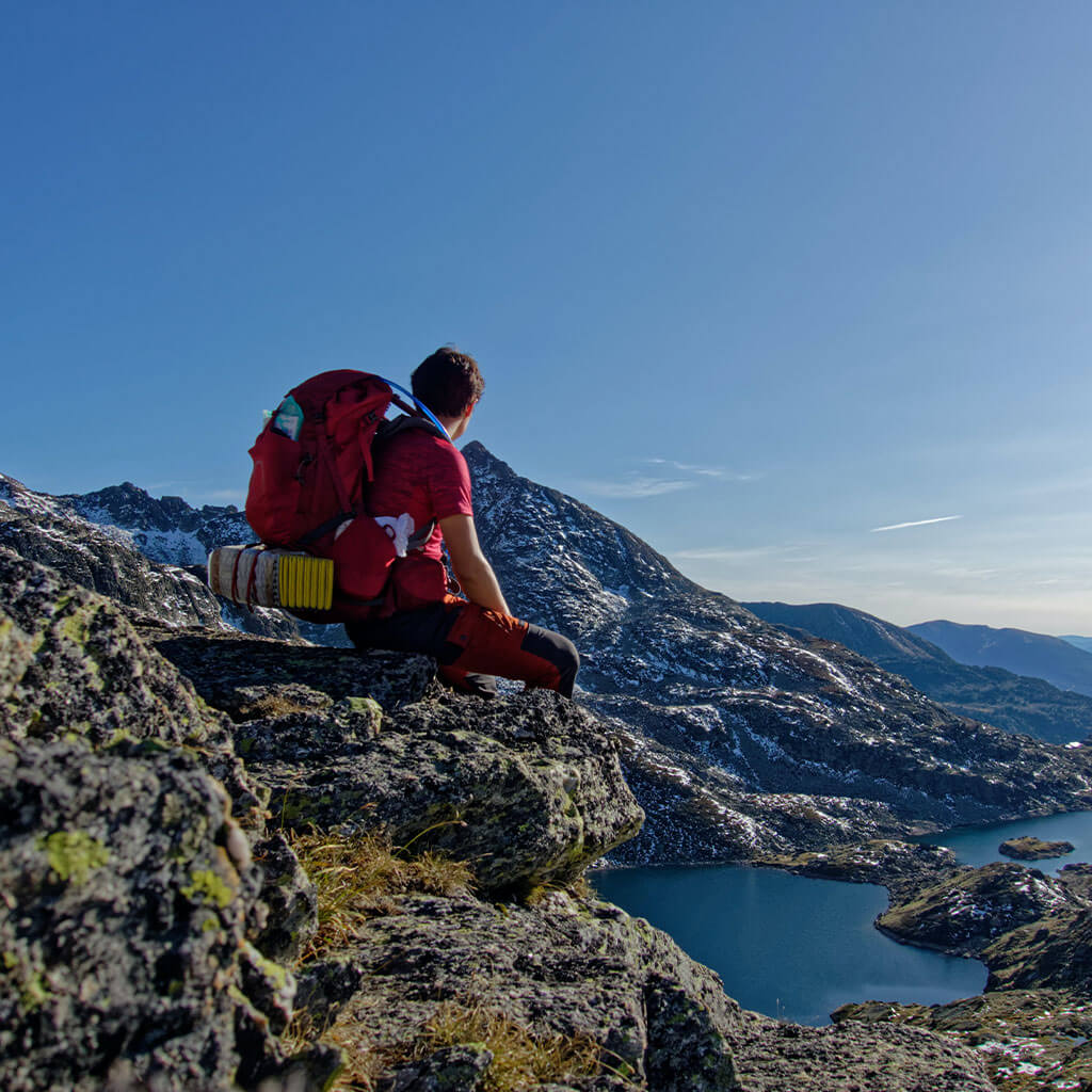 backpacker sitting on rocky edge overlooking view of mountain range and lake