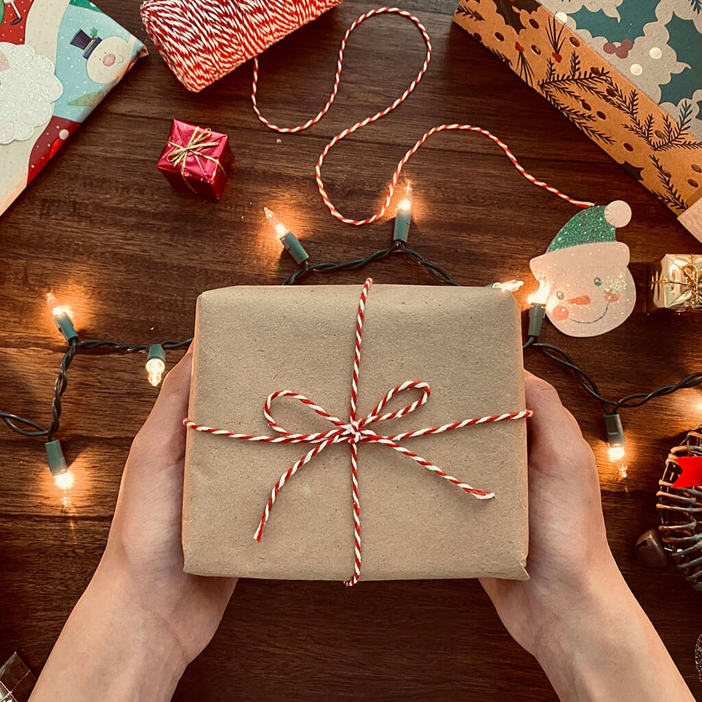 hands holding brown wrapped package with christmas lights in background
