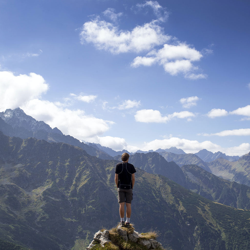 person standing on rock looking out at mountain range