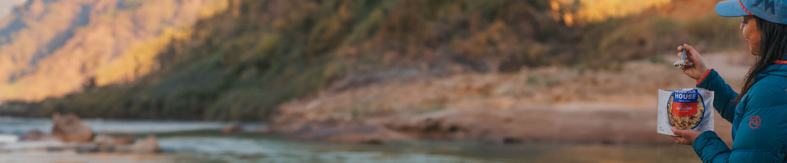 Person looking at a spoon of Mountain House Biscuits & Gravy smiling by a mountain river.