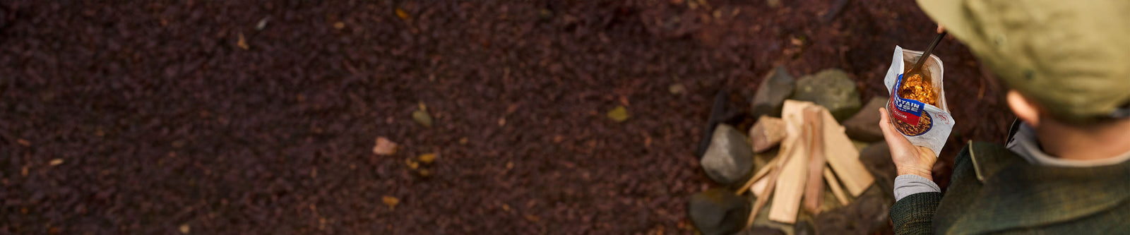 Looking over the shoulder of someone standing next to a firepit with closeup view of inside of Mountain House Beef Lasagna pouch.