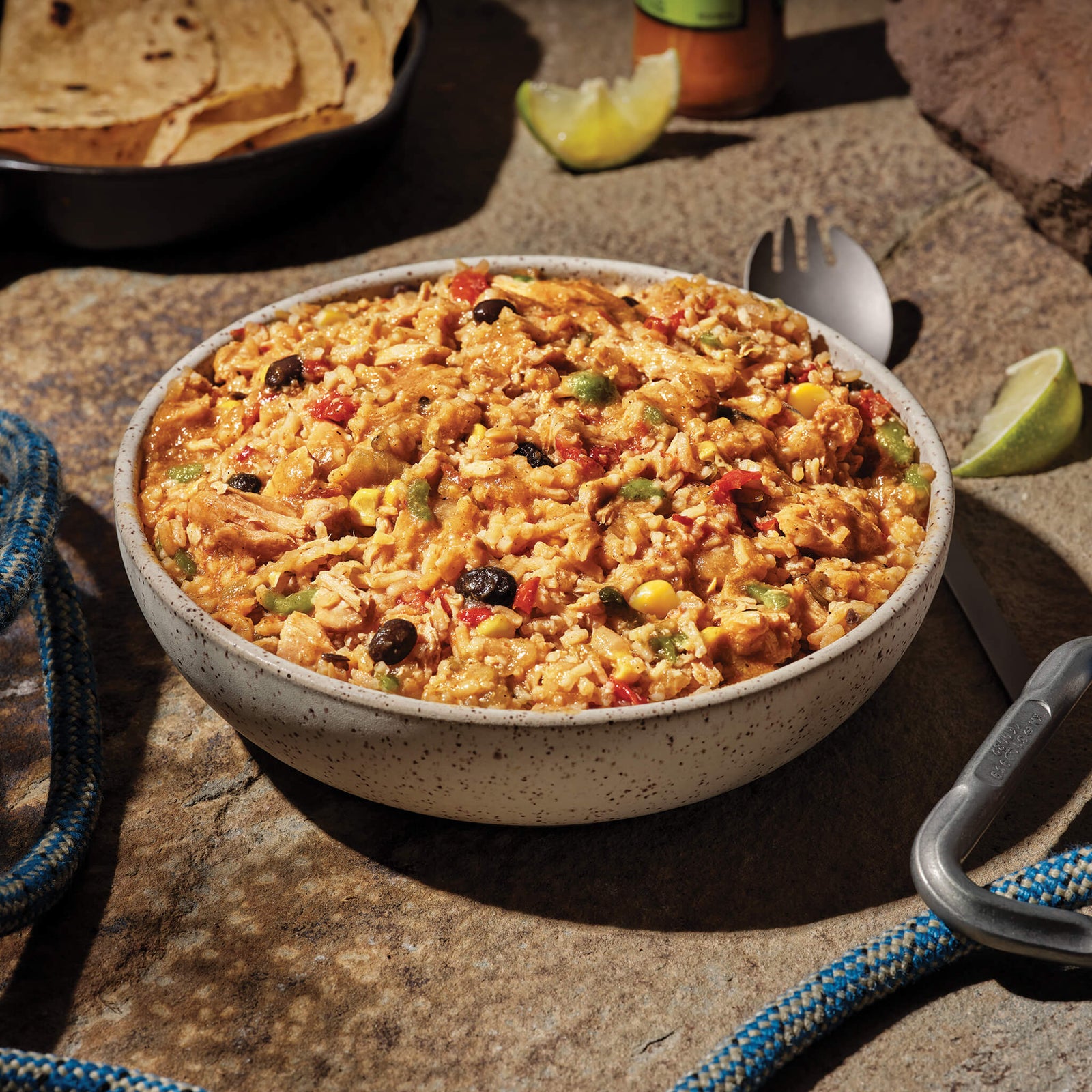 Bowl of Chicken Fajita with colorful vegetables on a stone surface with climbing equipment