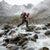 Man crossing rocky mountain river with trekking poles