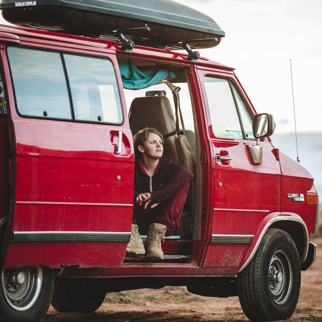 boy sitting in red camper van with door open gazing outside