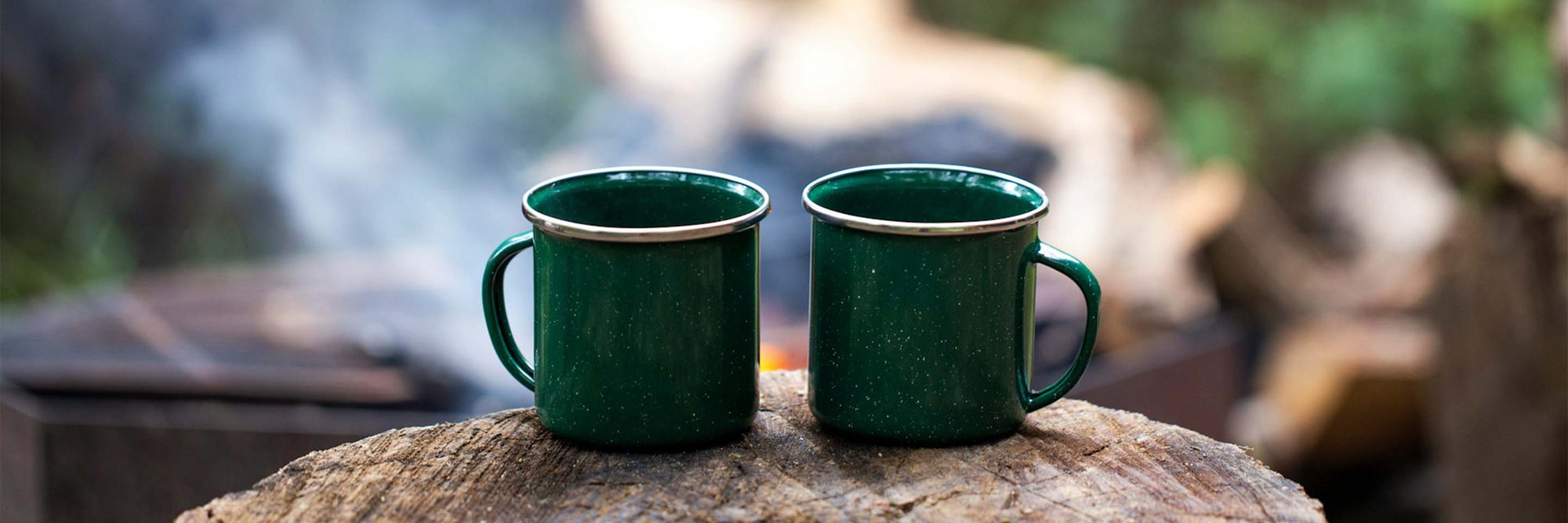 Two green coffee mugs in front of a campfire.