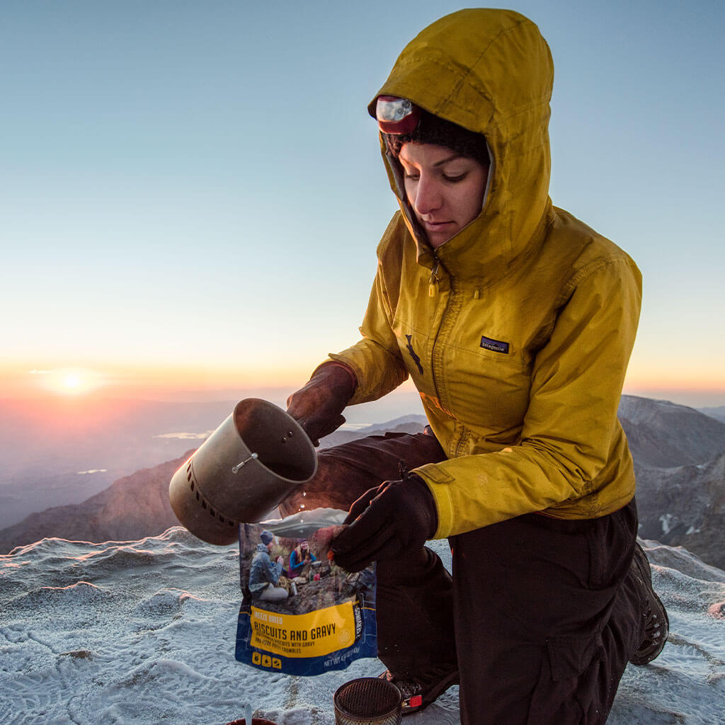 mountain climber pouring water in mountain house breakfast pouch on top of mountain