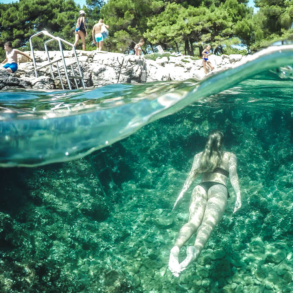 girl swimming underwater in lake while people sit up on rocks