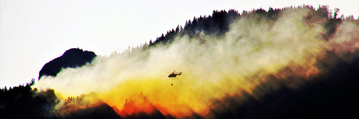 Helicopter flying over a forest wildfire and dropping water.