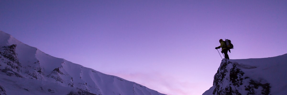 Trekker on a snowy mountain ridge with alpine peaks in the background.