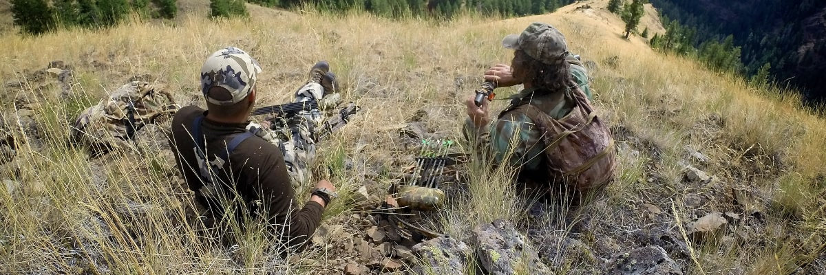 Group of hunters relaxing at a campsite with gear in the background.