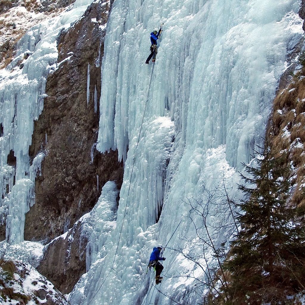 People ice climbing a large ice wall.