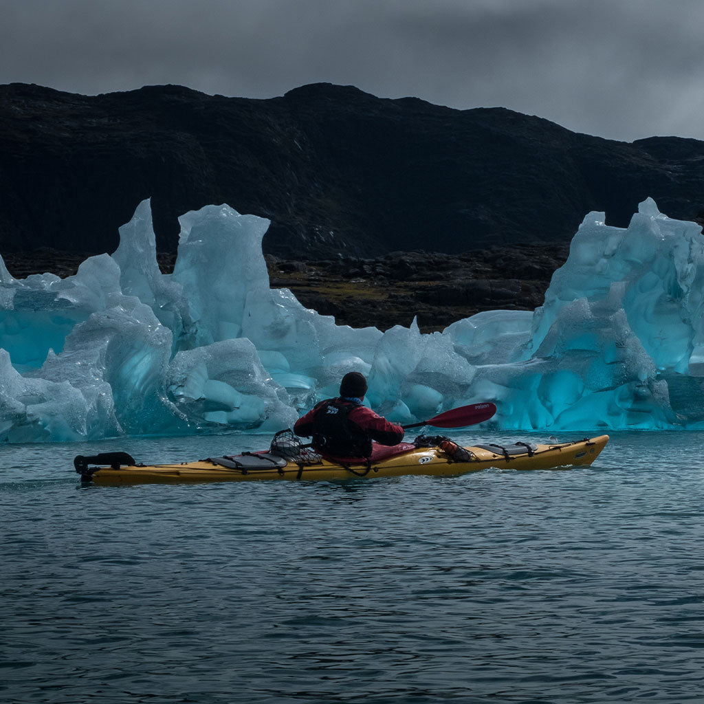 person kayaking in front of glacier
