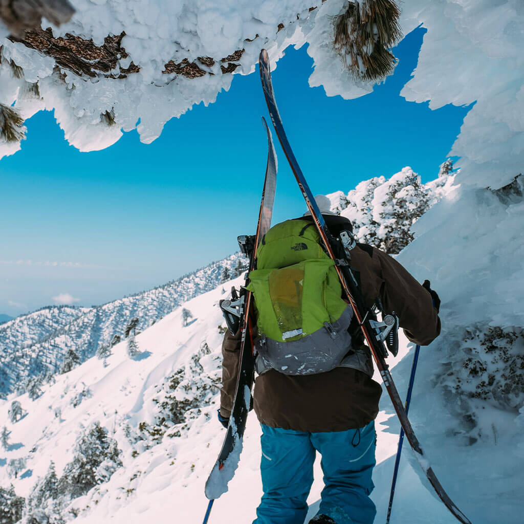 person wearing green backpack carrying skis through snow