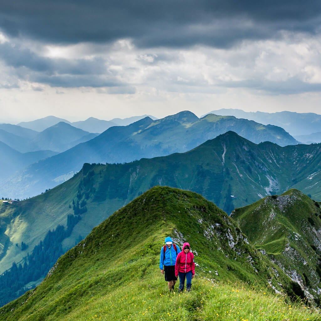 Two people hiking grassy mountain ridge