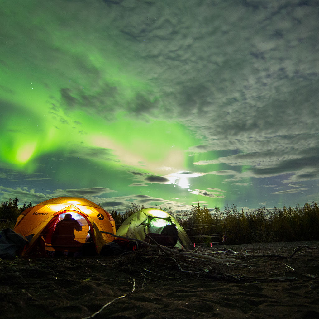 Two tents set up underneath northern lights during winter