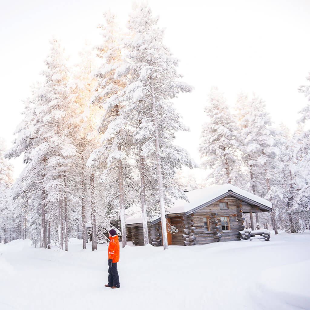 person standing in snow outside cabin while daylight