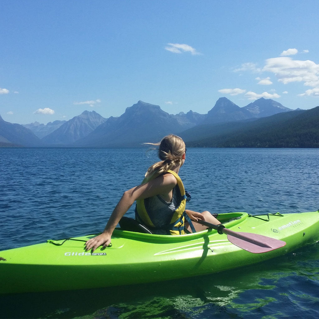 woman on kayak on body of water looking at mountains at glacier national park