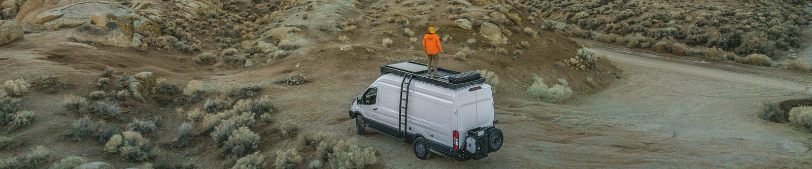 Man standing on top of campervan looking at desert mountain view.