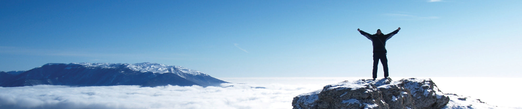 Person standing above the clouds on a mountain peak with arms spread out in victory.