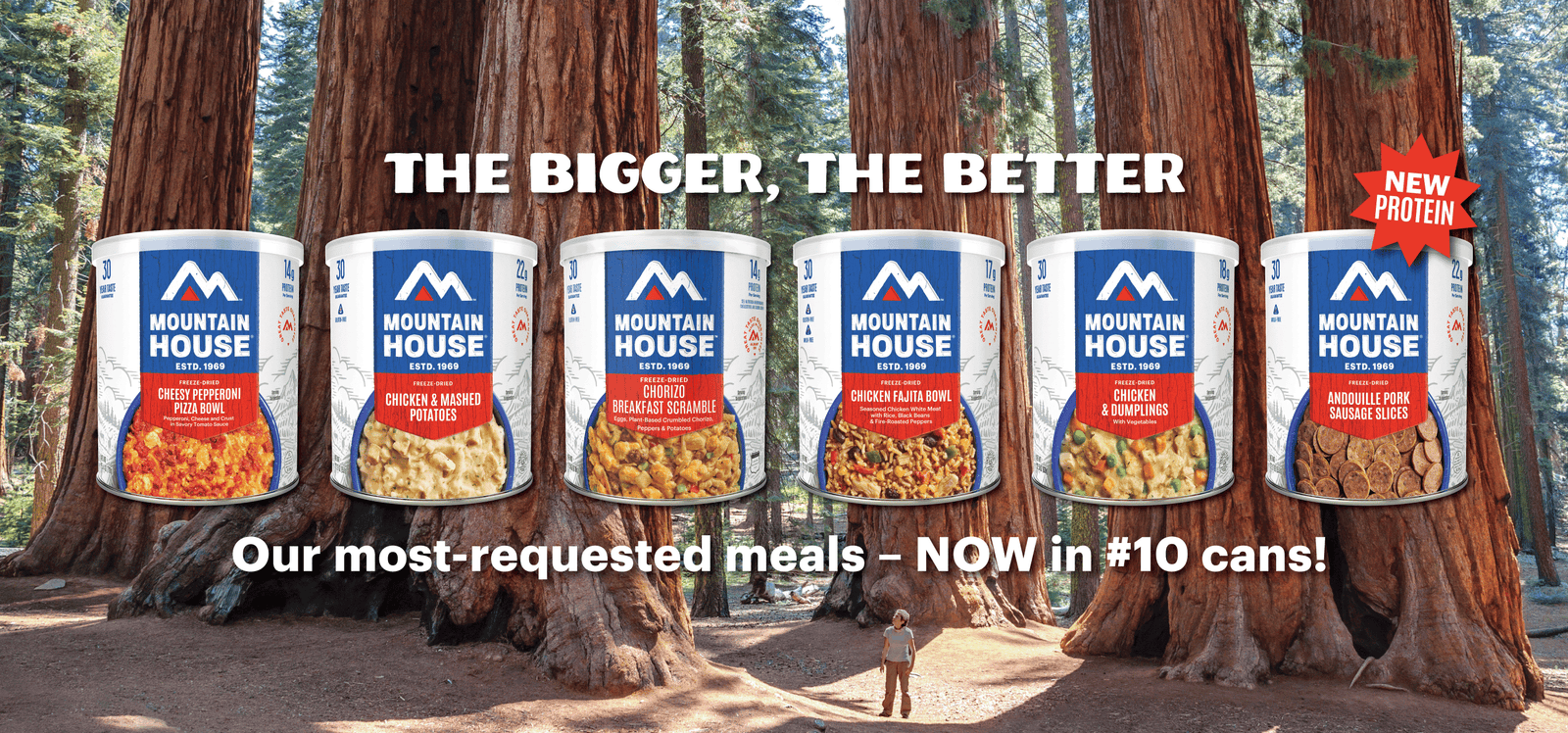 Six Mountain House #10 cans with a person looking up at redwoods. Text: "The Bigger, The Better. Our most-requested meals — NOW in #10 Cans." A starburst near the Andouille Pork Sausage Slices can says "New Protein."