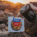 Person pouring hot water from Jetboil into a pouch of Mountain House Breakfast Skillet on a rocky beach.