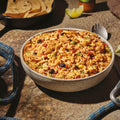 Bowl of rice., chicken, beans, and vegetables on a rustic surface with tortillas and a lime.