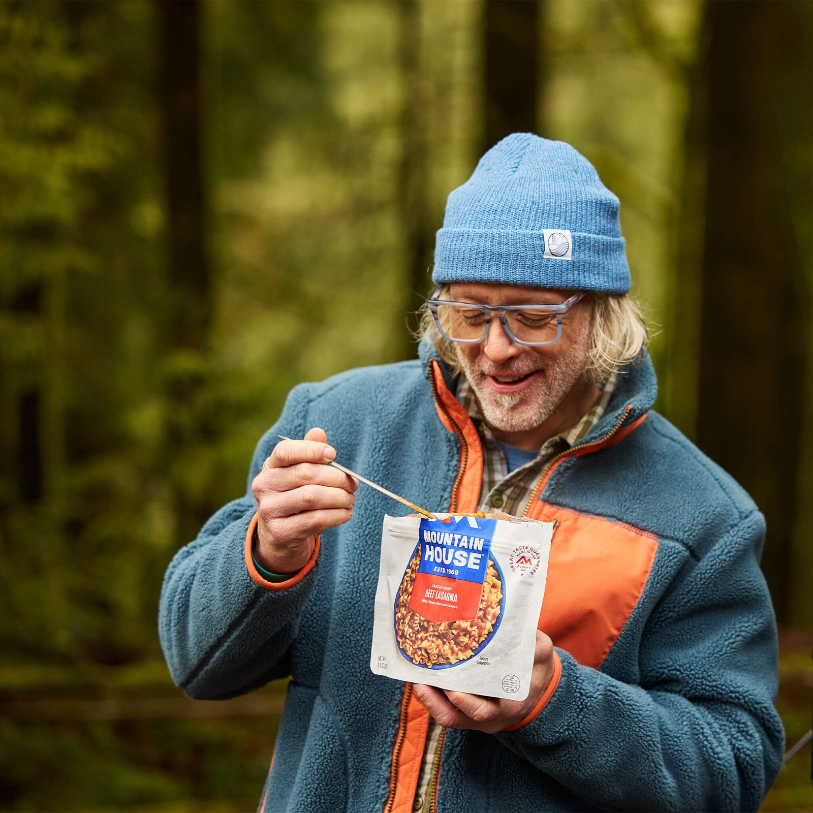 Person standing in the woods during the fall eating from a pouch of Mountain House Beef Lasagna.