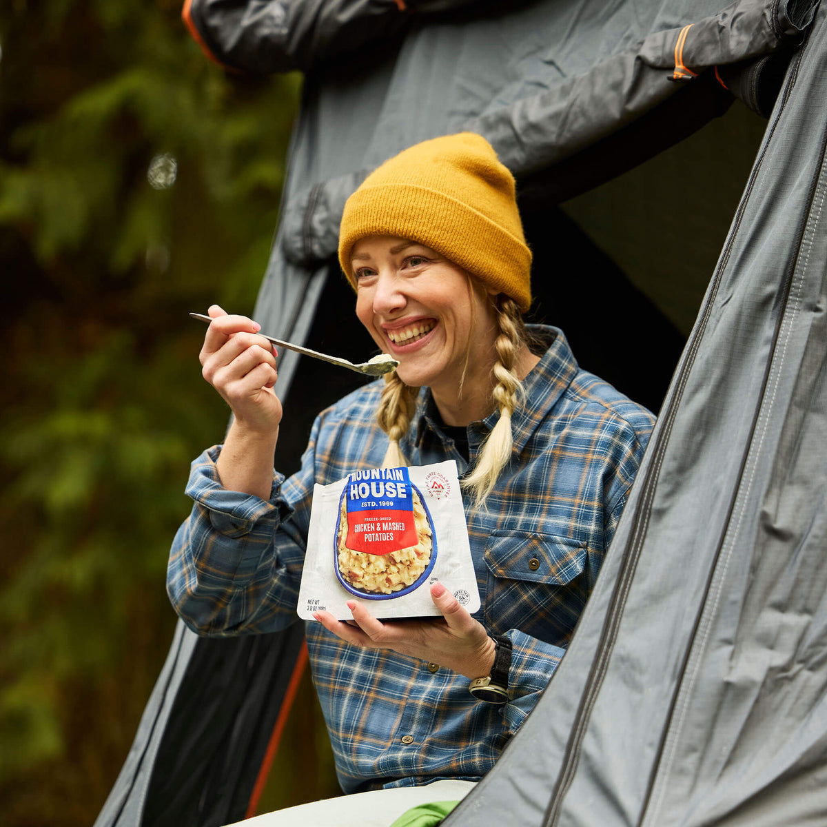 Gril sitting in roof tent taking a bite of Mountain House Chicken & Mashed Potatoes.