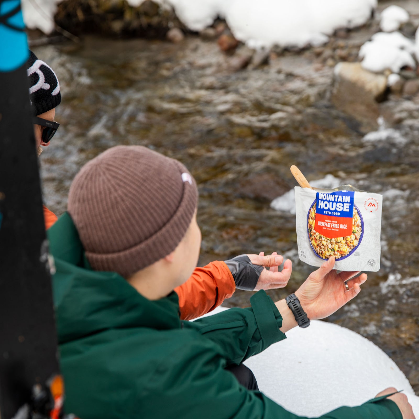 Person holding a Mountain House Breakfast Fried Rice pouch by a stream during winter