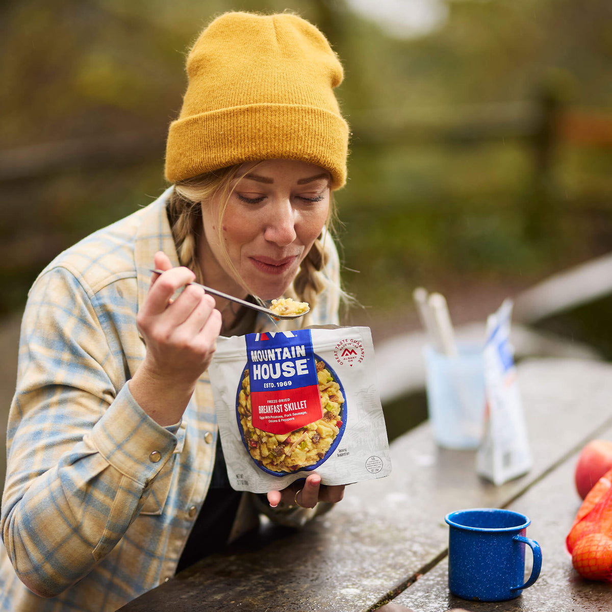 A girl sitting at a picnic table preparing to take a bite of Mountain House Breakfast Skillet, surrounded by colorful fall foliage.