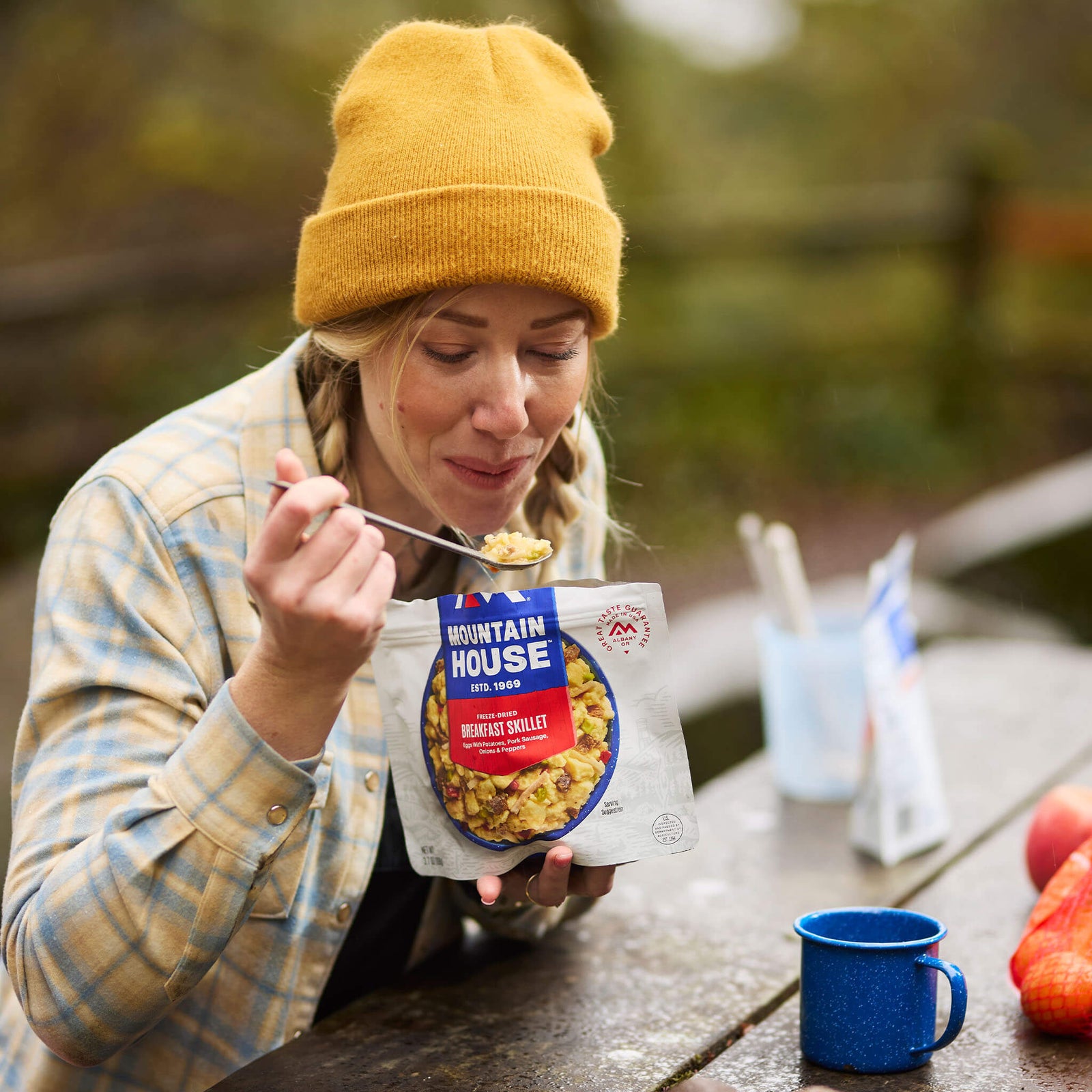 A girl sitting at a picnic table preparing to take a bite of Mountain House Breakfast Skillet, surrounded by colorful fall foliage.