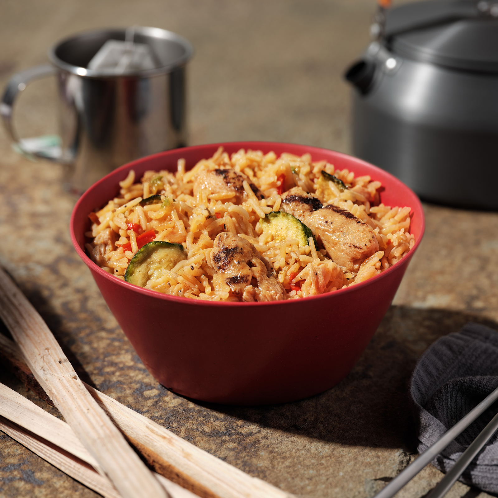 Bowl of Mountain House Kung Pao Chicken sitting on countertop with other camping supplies in the background.