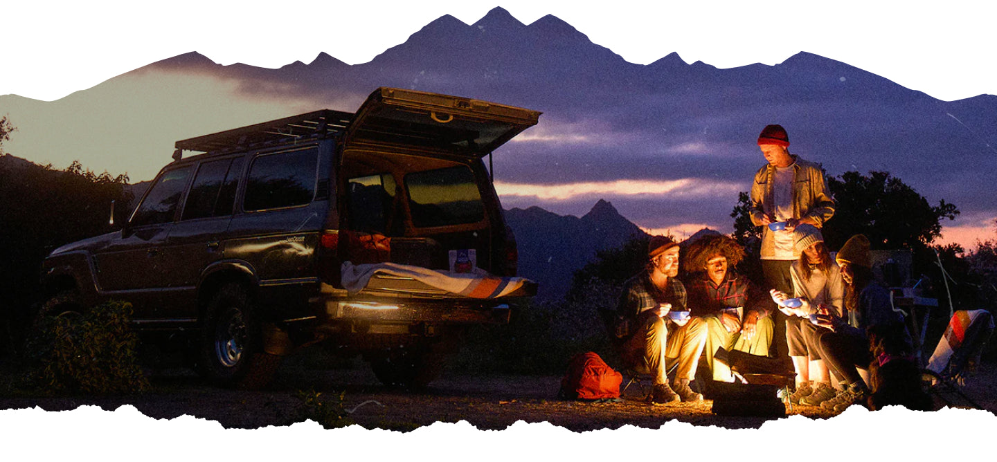 Five people around a campfire at night eating Mountain House meals