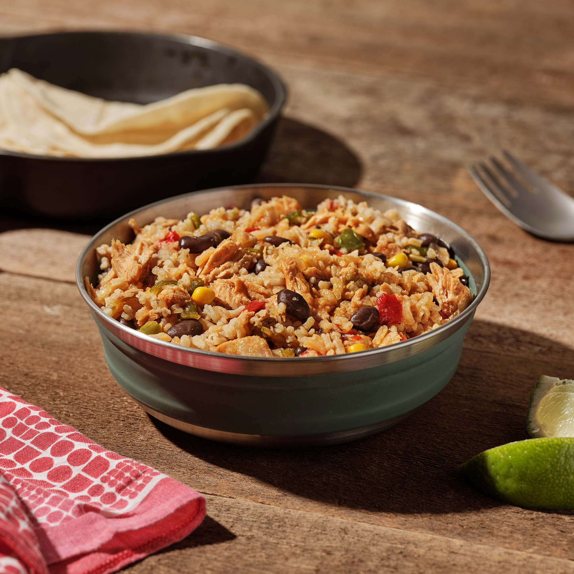 Mountain House Chicken Fajita Bowl in a metal camping bowl, with a lime and a cast iron skillet of tortillas nearby.