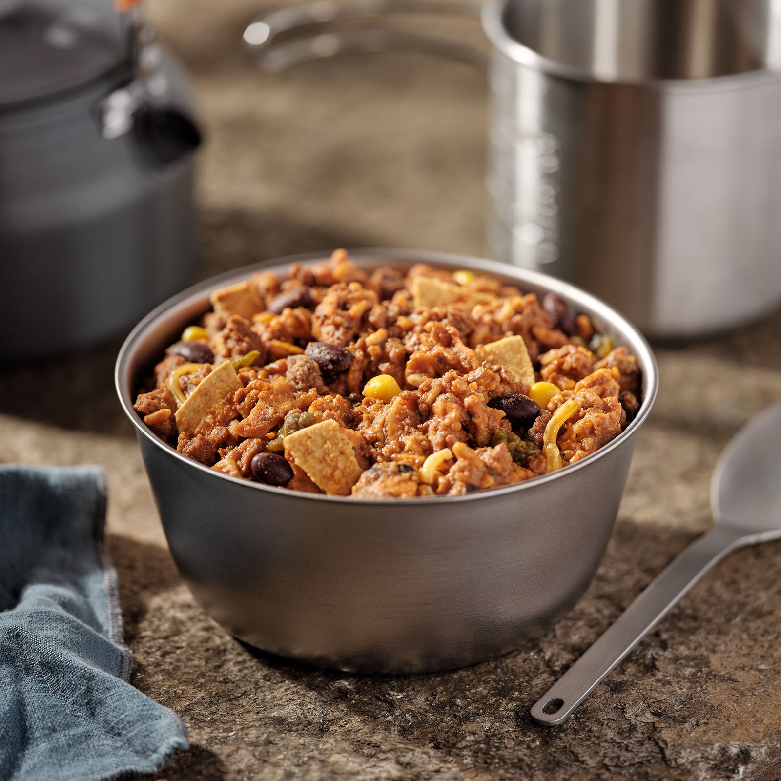 Mountain House Cheesy Beef Enchilada in a silver camping bowl next to other camping equipment.