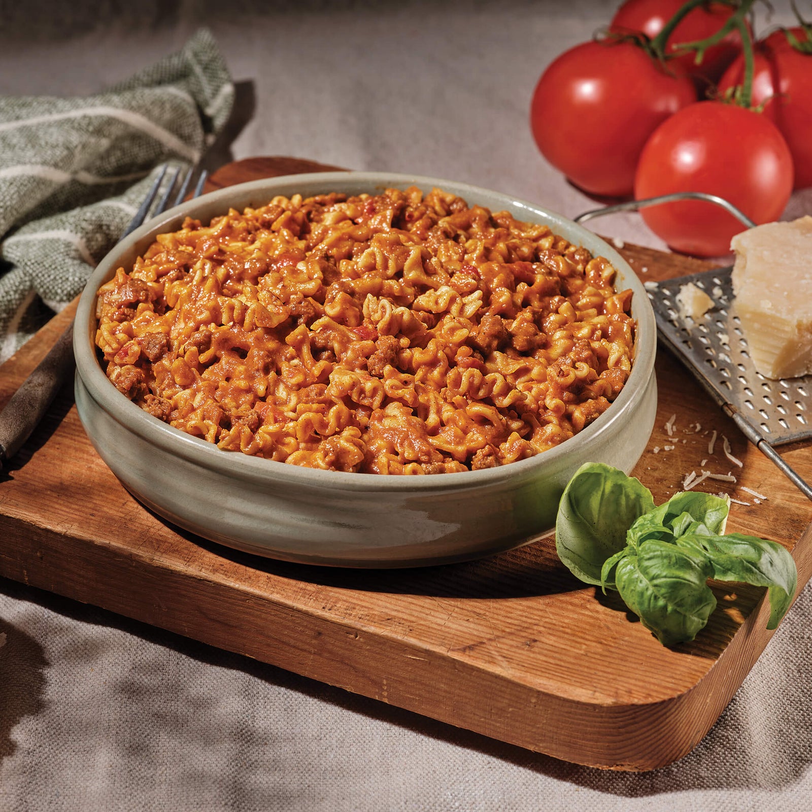 Bowl of lasagna pasta with tomato sauce on a wooden cutting board with tomatoes and basil.
