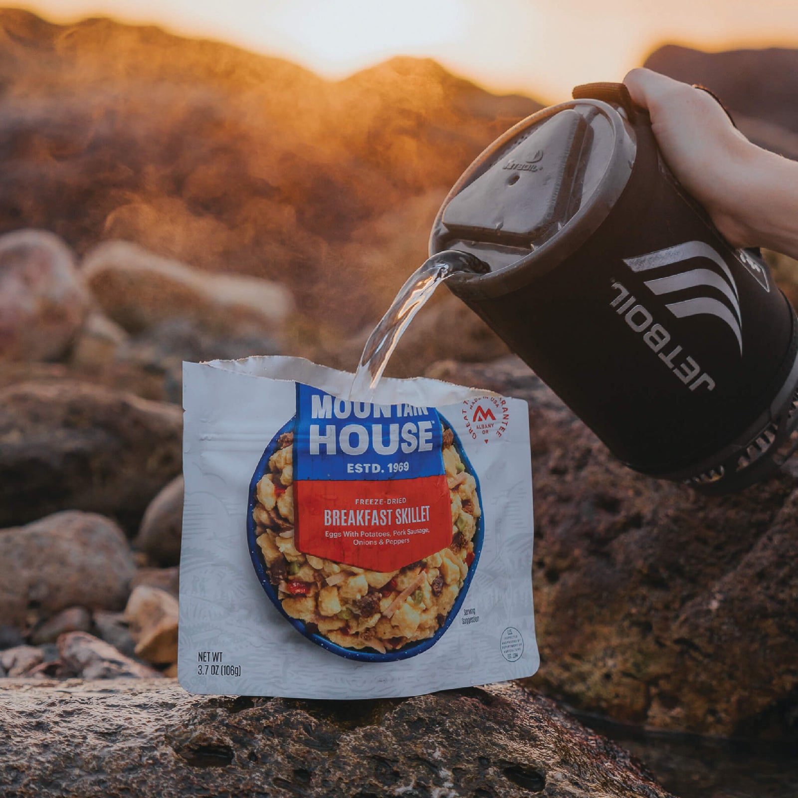 Person pouring hot water from Jetboil into a pouch of Mountain House Breakfast Skillet on a rocky beach.