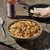 A bowl of Mountain House Breakfast Skillet on a rock surface, with a cast iron skillet of tortillas, hot sauce, and a fork behind it.