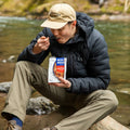 Guy eating from Cajun Jambalaya pouch next to river.