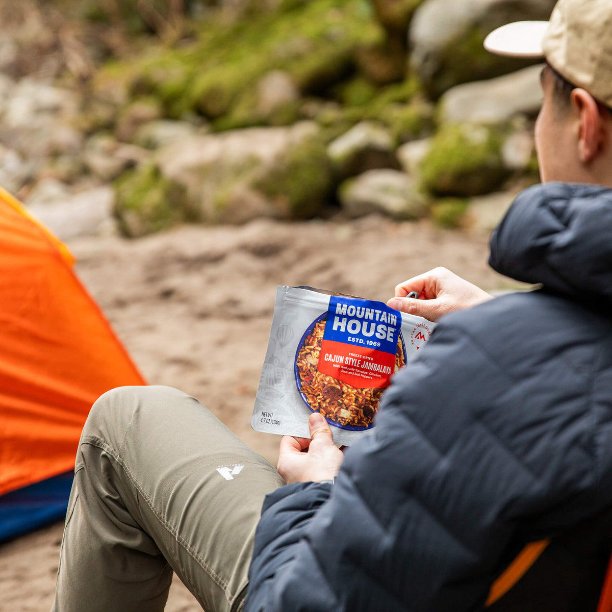 Person in a camping chair by a tent on a riverbank, eating Cajun Style Jambalaya.