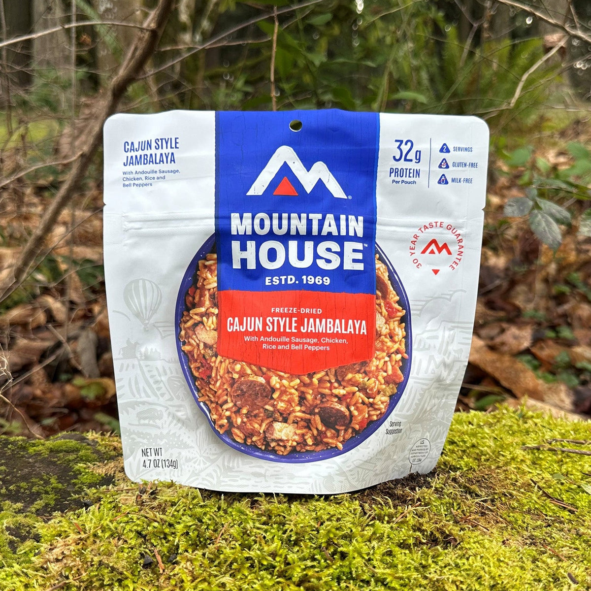 Mountain House Cajun Style Jambalaya pouch resting on a moss-covered rock, with a forest in the background.
