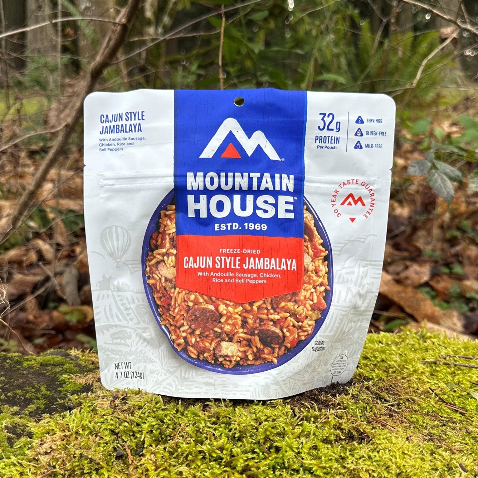 Mountain House Cajun Style Jambalaya pouch resting on a moss-covered rock, with a forest in the background.