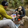 Two guys by a river preparing a pouch of Mountain House Chicken & Dumplings.