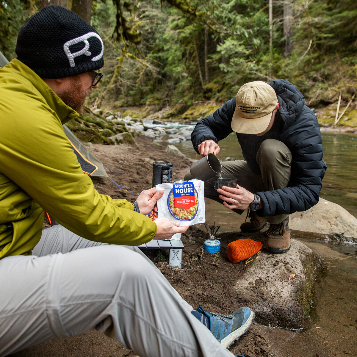 Two guys by a river preparing a pouch of Mountain House Chicken & Dumplings.
