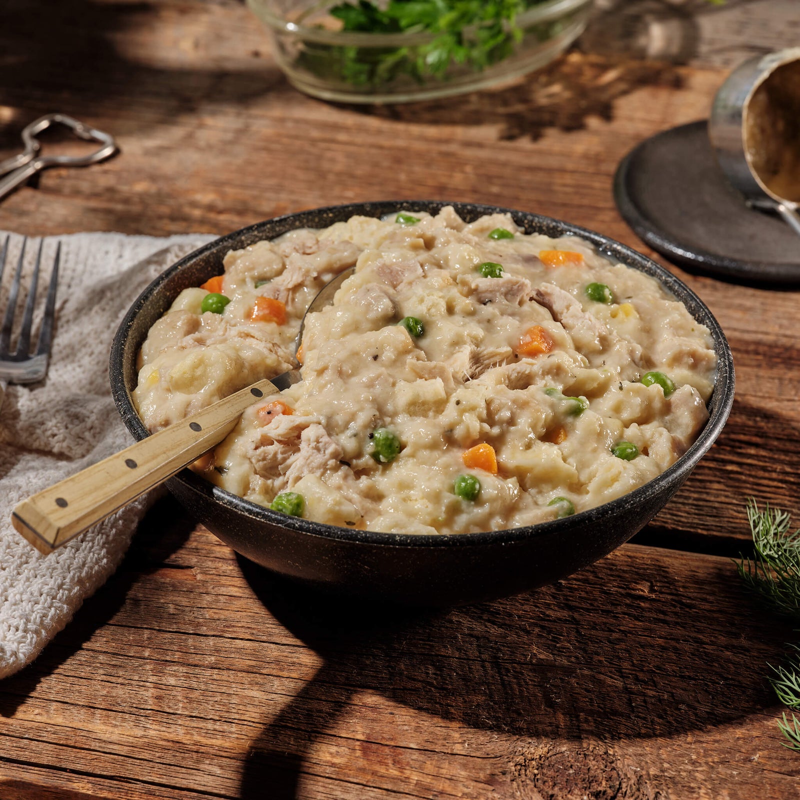 Bowl of creamy chicken and dumplings with vegetables on a wooden table