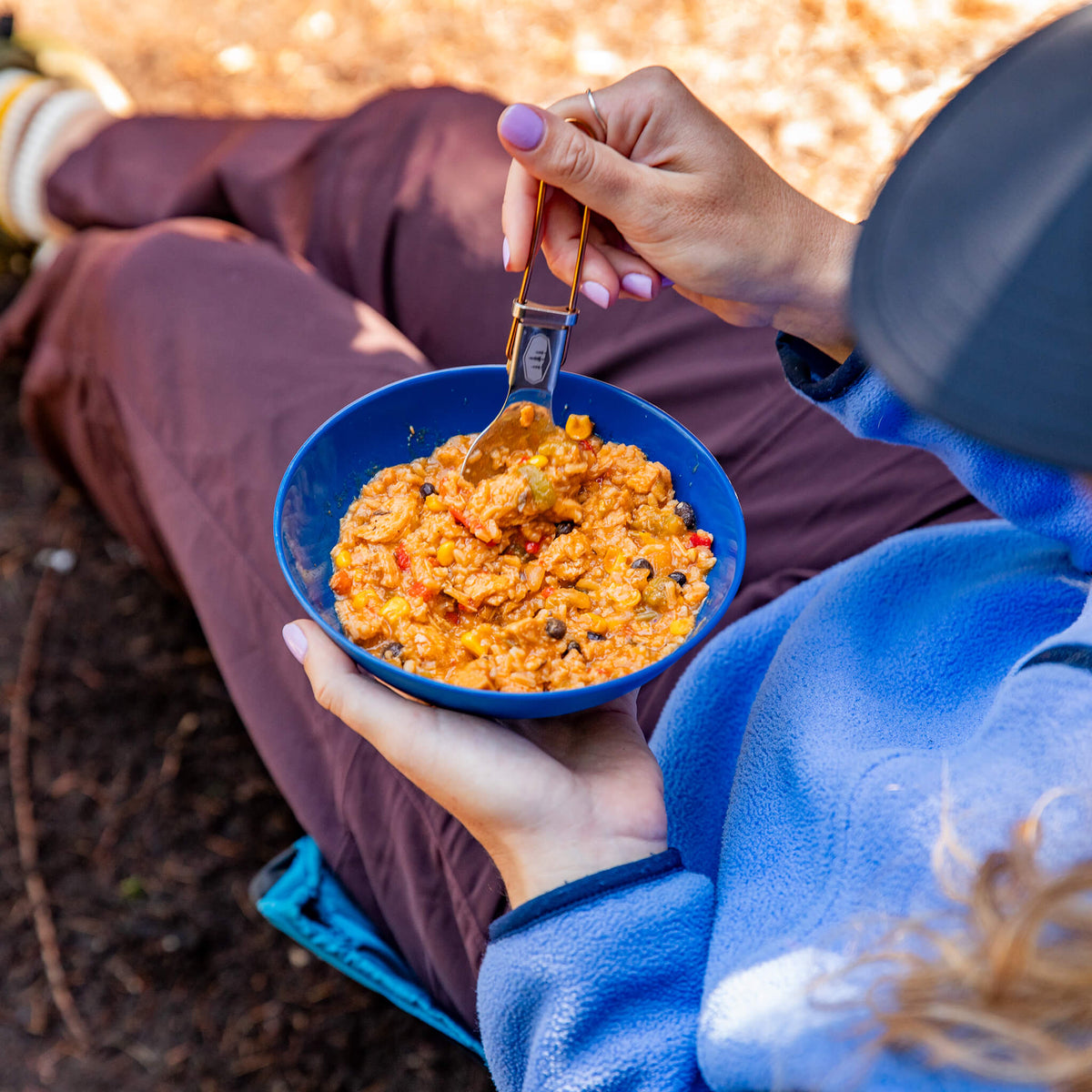 Person sitting in camping chair eating Chicken Fajita Bowl from a blue bowl.