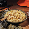 A bowl of Mountain House Fettuccine Alfredo with Chicken on a wooden countertop with hunting gear in the background.