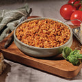 A bowl of Mountain House Beef Lasagna on a cutting board with tomatoes and parmesan cheese.