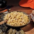 Dish of Fettuccine Alfredo with Chicken with a wooden spoon on a rustic wooden table with hunting equipment.