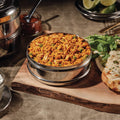 Bowl of Chicken Tikka Masala on chopping board next to bread.
